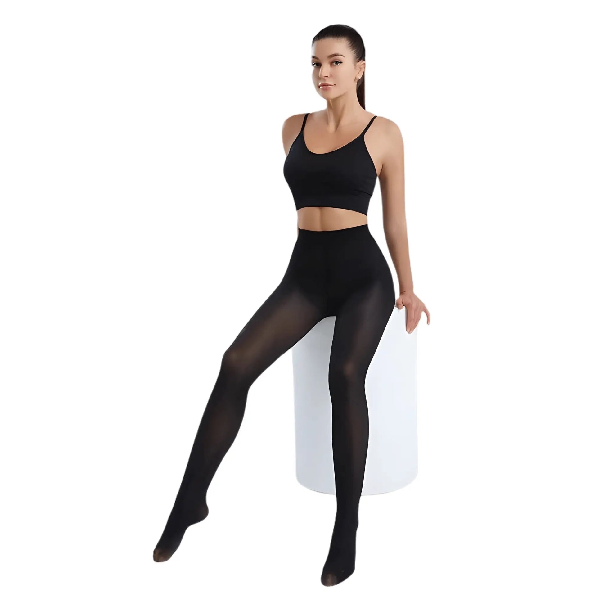 A full-body image of a female model wearing black ultra-sheer slimming tights and a black sports bra or crop top, sitting on a white circular pedestal.